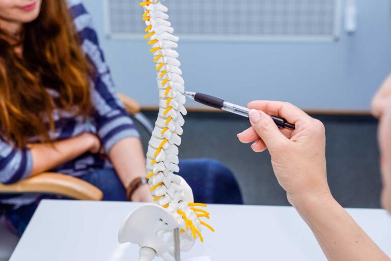 A chiropractor discusses a treatment plan with an adult patient beside an examination table.
