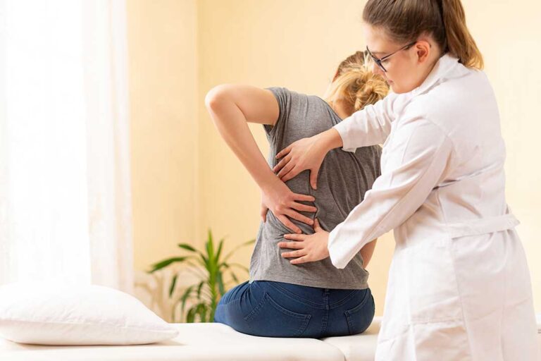 Person seated on an examination table while a clinician checks leg strength and sensation for back pain warning signs.