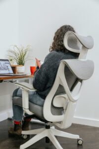 Person seated at a home desk with a raised monitor, supported back, relaxed shoulders, and feet flat on the floor.