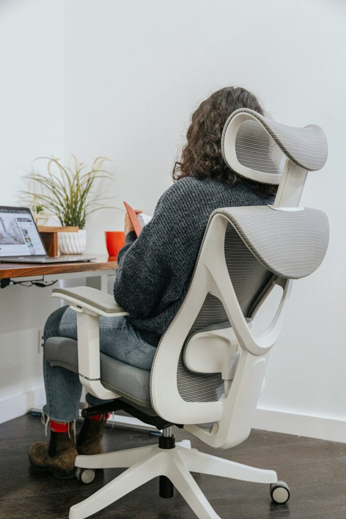 Person seated at a home desk with a raised monitor, supported back, relaxed shoulders, and feet flat on the floor.