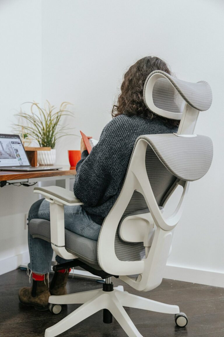 Person seated at a home desk with a raised monitor, supported back, relaxed shoulders, and feet flat on the floor.